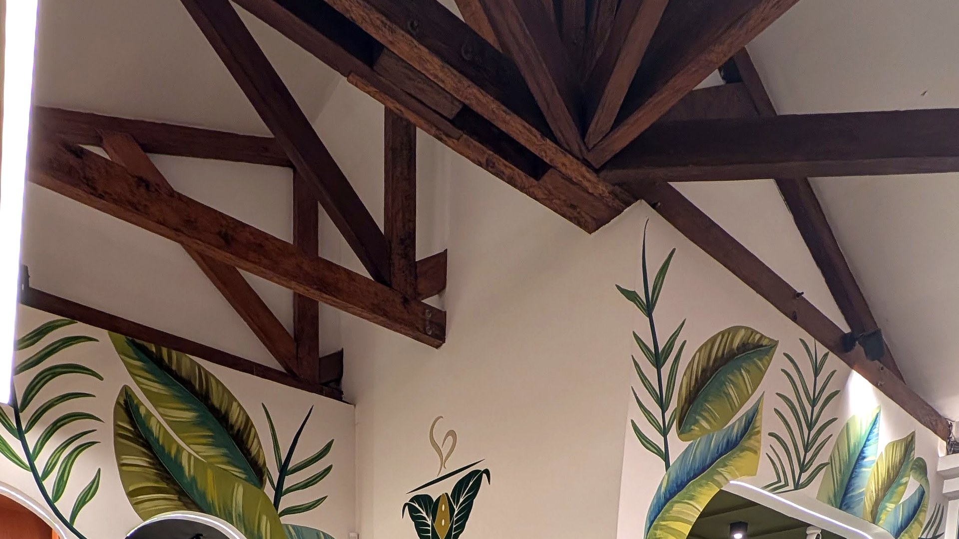 Techo con vigas de madera expuestas y murales de hojas tropicales pintadas en paredes blancas