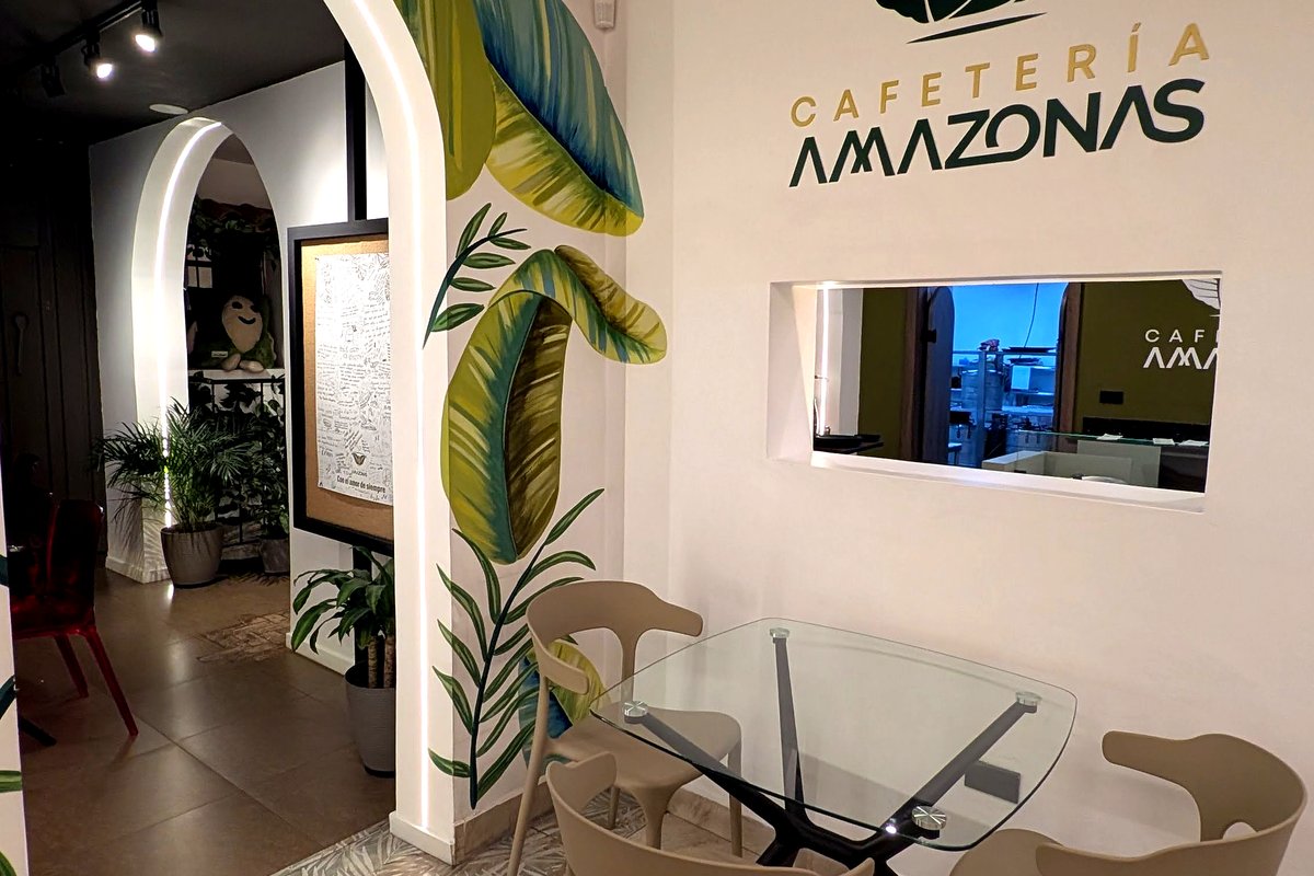 Area de comedor de Cafetería Amazonas con logo en pared, murales de hojas tropicales y arcos con iluminacion LED